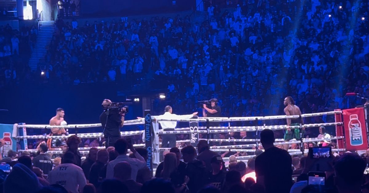 Un cuadrilátero de boxeo profesional iluminado durante una velada en un estadio colmado